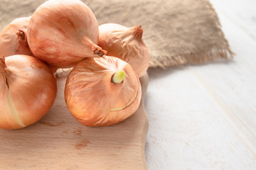 Burlap with yellow onions. Fresh onions on wooden background. Vegetables for a healthy diet.