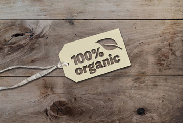 white hang tag cardboard lable with string attached an text 100 percent organic on rustic wooden table