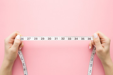 Woman's hand holding white measure tape on pastel pink background. Mock up for body slimming, weight loss or dressmaker's offer or other ideas. Empty place for text, logo or object. 