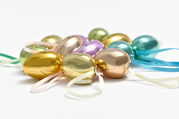 Shiny easter eggs in different pastel shades with ribbon on a white background.