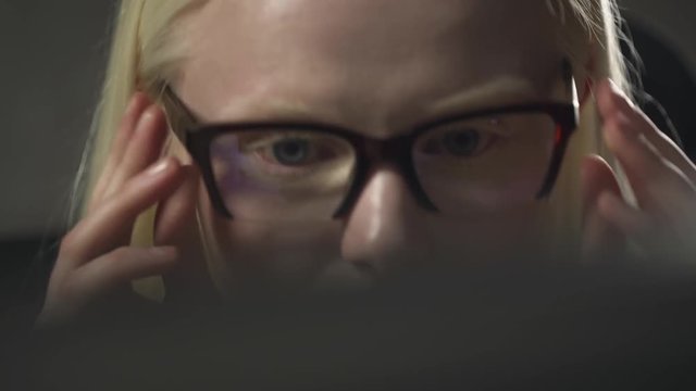Young manager girl puts on glasses, working at computer in office, closeup of albino girl eyes, reflections on the glasses, looking at screen of computer.