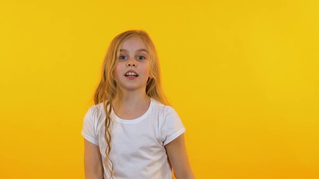 Cheerful girl dancing funny dance on isolated yellow background, slow-motion