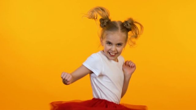 Active female child fooling around, dancing and jumping on bright background