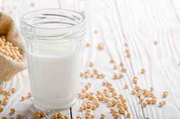 Non-dairy alternative Soy milk or yogurt in mason jar on white wooden table with soybeans in hemp sack