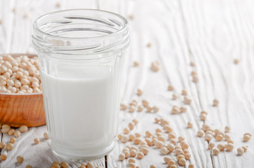 Non-dairy alternative Soy milk or yogurt in mason jar on white wooden table with soybeans in bowl aside