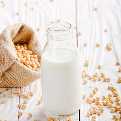 Non-dairy alternative Soy milk or yogurt in glass bottle on white wooden table with soybeans in hemp sack