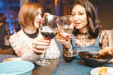 Two girl friends have fun and chat while drinking a glass of wine in a restaurant in a nightclub. The concept of relaxing and frienship