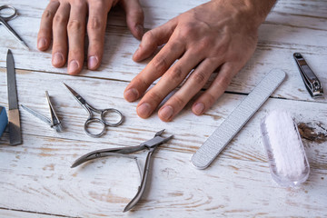 Male hands on a white table with manicure tools and instruments. Top view, close-up.