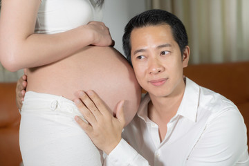 Asian husband listening to sound baby in belly wife.