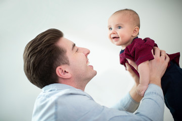Father Lifting Smiling Baby Son Into Air At Home As They Play Gane Together