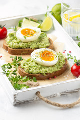 Toast with avocado puree and soft-boiled egg on white tray, liquid yolk, delicious breakfast, light sandwich. Healthy food