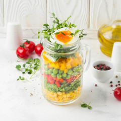 Fresh salad in jar with soft boiled egg, liquid yolk. Corn, green lettuce, bell pepper, peas. Delicious food, healthy lunch