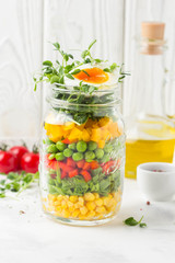 Fresh salad in jar with soft boiled egg, liquid yolk. Corn, green lettuce, bell pepper, peas. Delicious food, healthy lunch