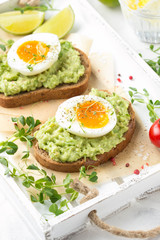 Toast with avocado puree and soft-boiled egg on white tray, liquid yolk, delicious breakfast, light sandwich. Healthy food