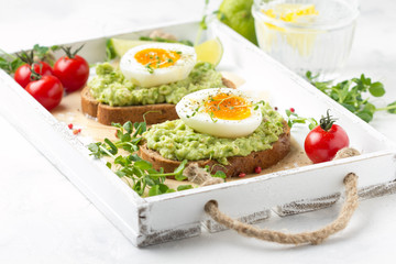 Toast with avocado puree and soft-boiled egg on white tray, liquid yolk, delicious breakfast, light sandwich. Healthy food