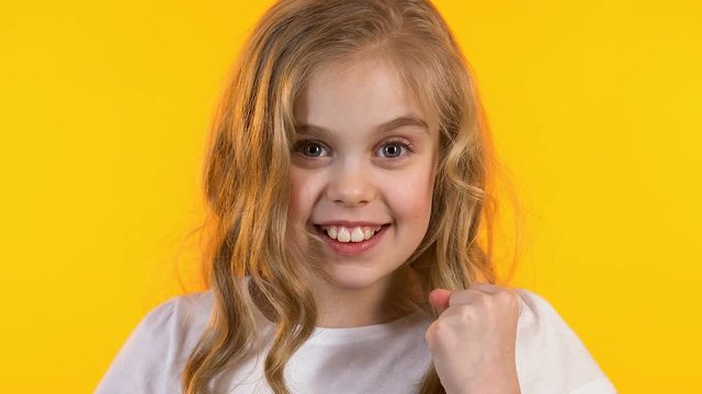 Surprised girl showing yes gesture satisfied with her victory, yellow background