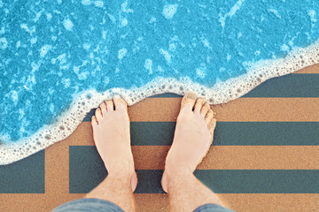 Feet on sandy beach with flag. Top View on Wave