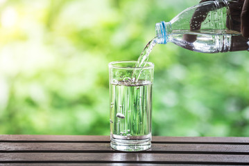 Drink water pouring into glass on wooden table over sunlight with natural lighting and background