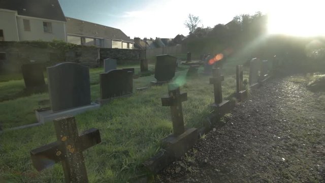Slow pan through abandoned grave yard in Ireland with sun flar coming through clouds
