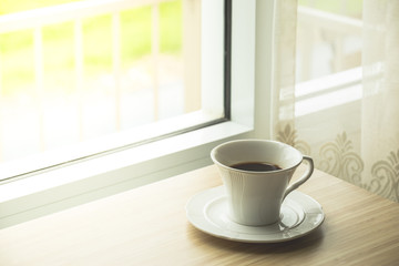 Cup of coffee on wooden by the window. Coffee break in morning and sunlight