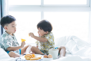 Brothers are sharing breakfast on the bed in the morning.