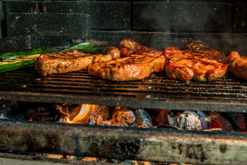 Juicy pork steaks roasting on charcoal barbecue with few pumpkins beside them.