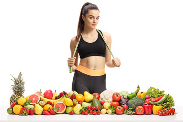 Young sporty female with a skipping rope around her neck standing behind a pile of fruits and vegetables