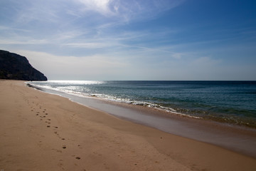sand on the beach with blue sky and rocks in the background