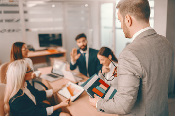 Businessman having in formal wear having presentation in boardroom. Colleagues listening to him and asking questions. Practicing the Golden Rule is not a sacrifice; it is an investment.