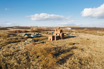 Aerial view of abandoned russian orthodox church made of stone in Nazaryevka village among dry grass fields, little snow patches and trees on a sunny spring evening. Penza oblast, Russia
