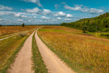 Fototapeta na wymiar The dirt road in the field on the flat area in sunny day with clouds in the sky