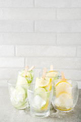 Healthy diet summer dessert, Vegan trendy ice cream. Sweet and sour infused water popsicles with cucumber, lime and lemon slices, Grey stone background copy space