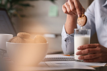 Close up of businesswoman dipping cookie in glass of milk.