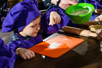 cute little boy with chef hat standing at table kneading bread dough