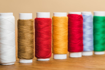 colorful cotton thread coils in row on wooden table isolated on beige