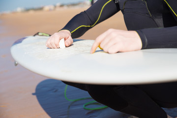 Closeup of young man waxing surfboard on sunny beach