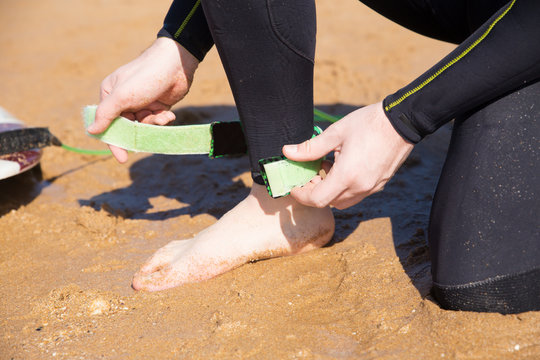 Closeup of young man putting on surfboard leash on sand