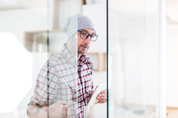 Portrait of fashionable architect or designer with tablet device opening glass office door.