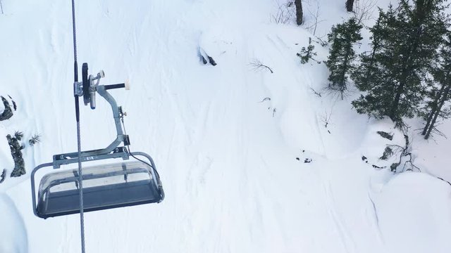 Aerial view of a two-seat cable car above the man snowboarding on a track in the coniferous forest. Footage. Ski resort