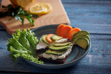 Dark burger with grain bread on dark ceramic plate, salad, rosemary and lemon