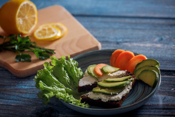 Dark burger with grain bread on dark ceramic plate, salad, rosemary and lemon