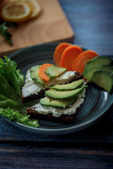 Dark burger with grain bread on dark ceramic plate, salad, rosemary and lemon