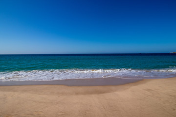golden sand, soft waves with white foam, sea and blue sky