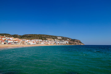 Fototapeta na wymiar soft waves with white foam in the foreground, in the background the village of Sesimbra