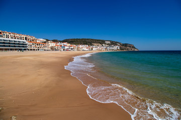 soft waves with white foam in the foreground, in the background the village of Sesimbra