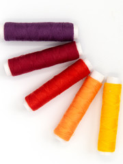 sewing threads in yellow, orange, red and purple isolated on white background, arranged in a semicircle