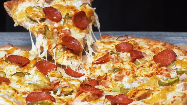 Close-up of chef's hands in silicone gloves taking a piece of delicious fresh Neapolitan pizza with circles of saveloy and cheese. Frame. Italian food