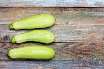 three fresh raw zucchini on an old wooden table with copy space, top view