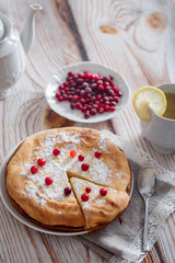 Cheesecake with cranberries and sugar, green tea and lemon on wooden table