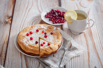 Cheesecake with cranberries and sugar, green tea and lemon on wooden table